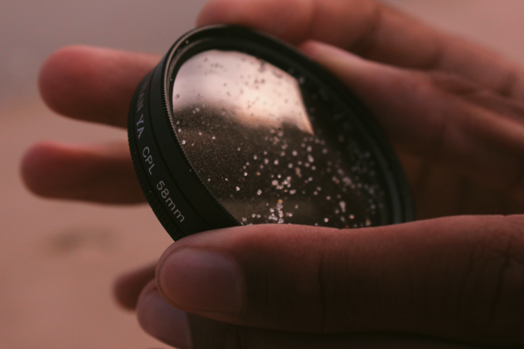 A person holds a dusty camera lens close up, capturing a detail-oriented moment.