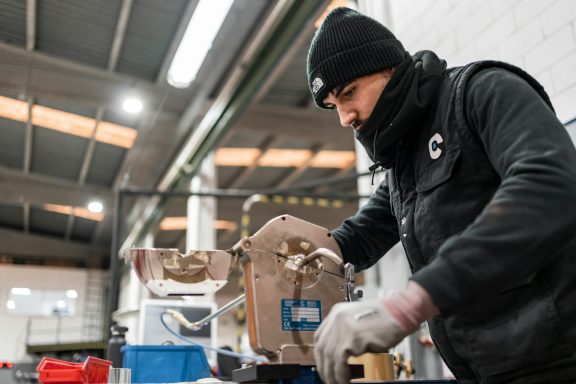 Ein Arbeiter bearbeitet ein Metallstück in einer Industrieumgebung.